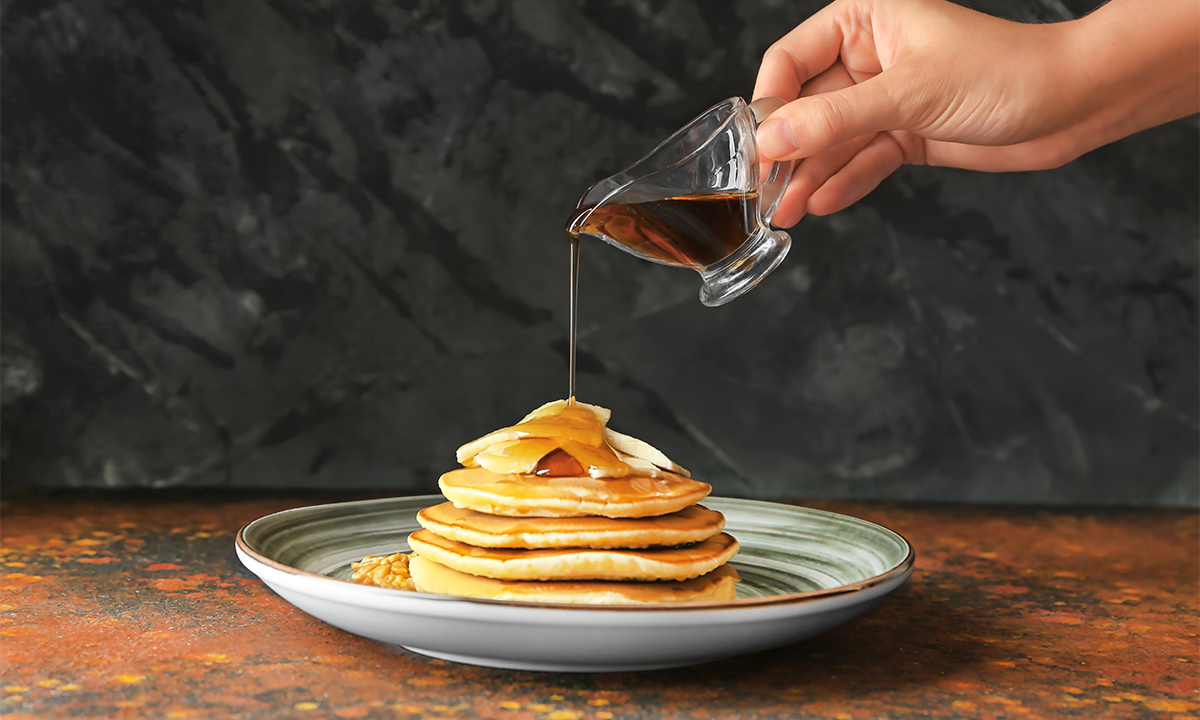 Woman pouring syrup onto pancakes.